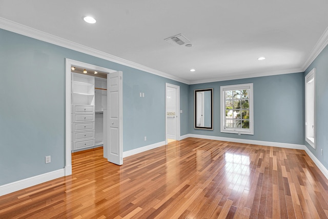 unfurnished bedroom featuring crown molding, visible vents, baseboards, light wood-type flooring, and a spacious closet