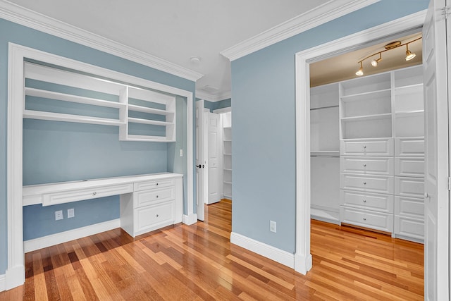 unfurnished bedroom featuring baseboards, ornamental molding, built in study area, and light wood-style floors