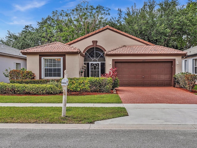 mediterranean / spanish house featuring an attached garage, stucco siding, a tiled roof, and driveway