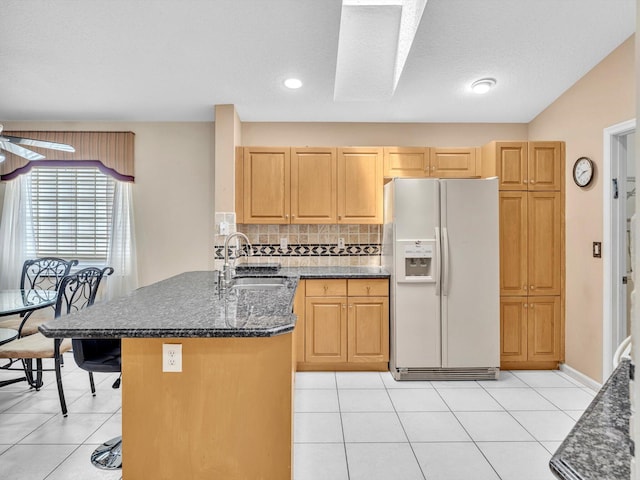 kitchen featuring a sink, white fridge with ice dispenser, a peninsula, decorative backsplash, and light tile patterned floors