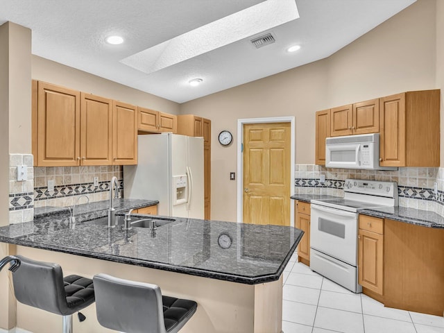 kitchen with visible vents, a sink, a peninsula, lofted ceiling with skylight, and white appliances