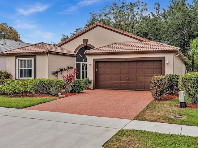 mediterranean / spanish-style home with a tiled roof, an attached garage, driveway, and stucco siding