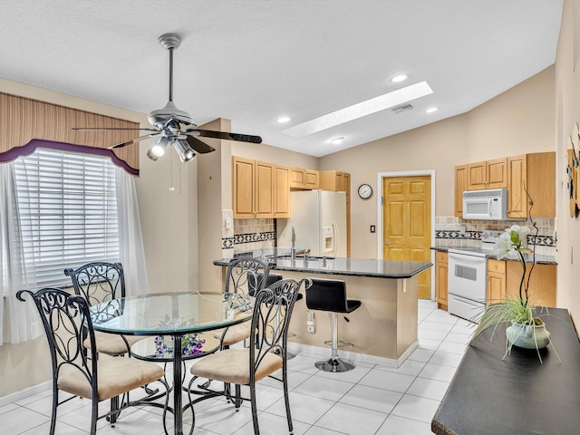 dining room with visible vents, a ceiling fan, light tile patterned floors, and vaulted ceiling with skylight