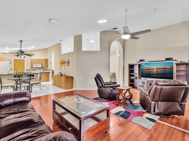 living area featuring arched walkways, a ceiling fan, visible vents, and light wood-style floors