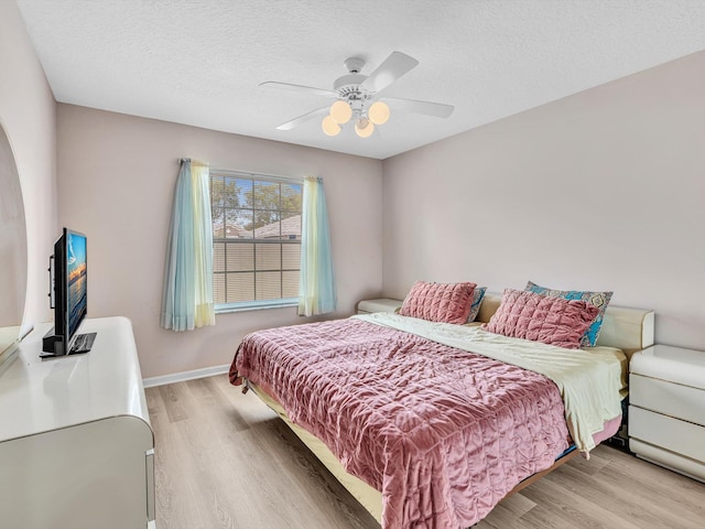 bedroom with a textured ceiling, ceiling fan, baseboards, and light wood-style flooring