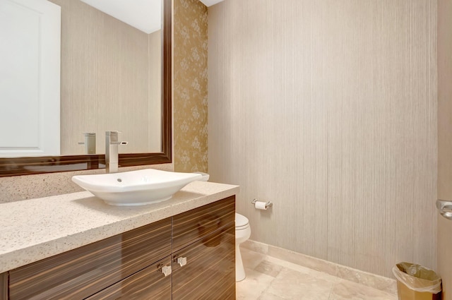 half bath with baseboards, wallpapered walls, toilet, and vanity