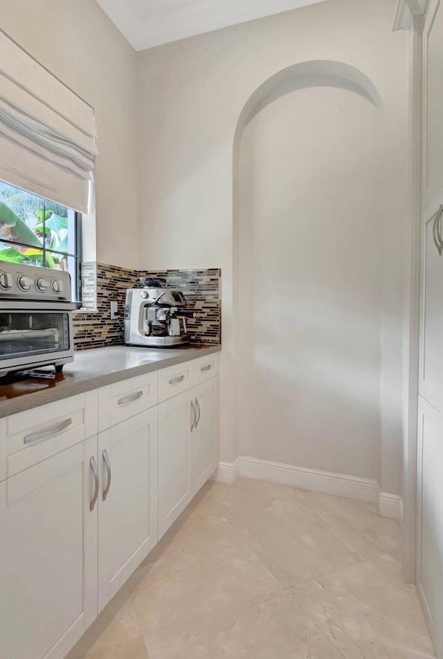 kitchen featuring tasteful backsplash, baseboards, a toaster, arched walkways, and white cabinets