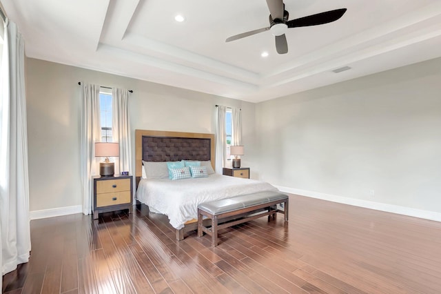 bedroom with recessed lighting, a tray ceiling, visible vents, baseboards, and wood finished floors