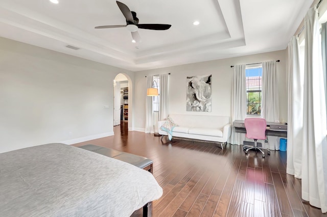 bedroom featuring visible vents, a tray ceiling, baseboards, arched walkways, and wood finished floors