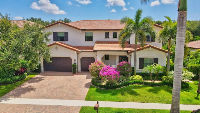 mediterranean / spanish-style home featuring a front yard, stucco siding, decorative driveway, a tiled roof, and an attached garage