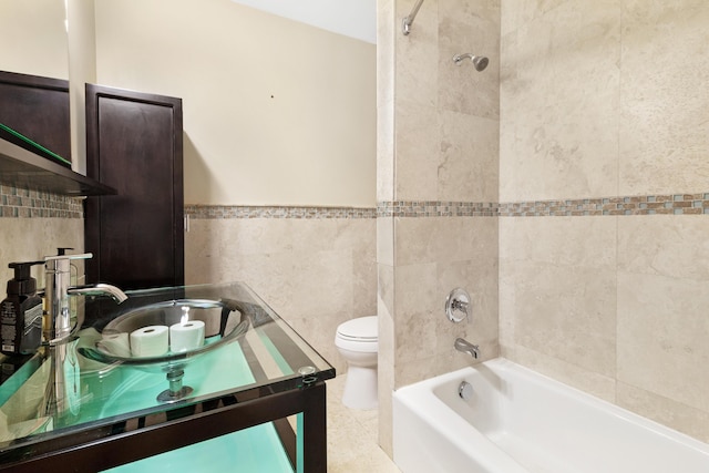 bathroom featuring vanity, toilet, a wainscoted wall, tile walls, and shower / washtub combination