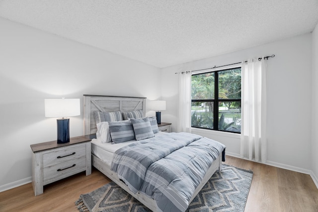 bedroom with baseboards, a textured ceiling, and light wood-style flooring
