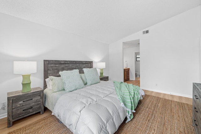 bedroom with lofted ceiling, wood finished floors, visible vents, and baseboards