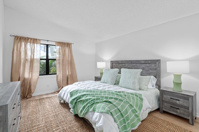 bedroom with a textured ceiling, light wood finished floors, and vaulted ceiling