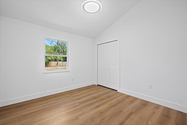 empty room featuring baseboards, light wood-style flooring, and lofted ceiling