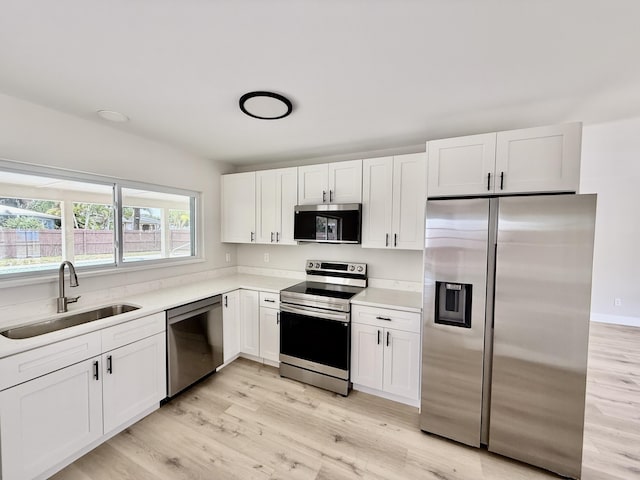 kitchen with a sink, light wood-style flooring, white cabinets, and stainless steel appliances