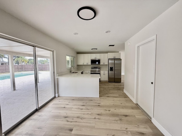 kitchen featuring white cabinets, appliances with stainless steel finishes, a sink, light wood-style flooring, and a peninsula