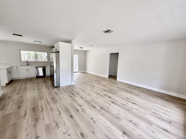 unfurnished living room featuring a sink, baseboards, light wood-style flooring, and visible vents