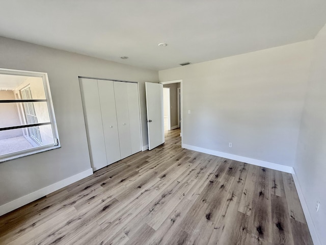 unfurnished bedroom with baseboards, a closet, wood finished floors, and visible vents