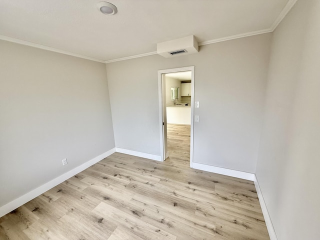 spare room with baseboards, ornamental molding, light wood-style flooring, and visible vents