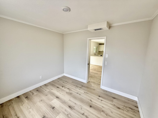 spare room with baseboards, ornamental molding, and light wood finished floors