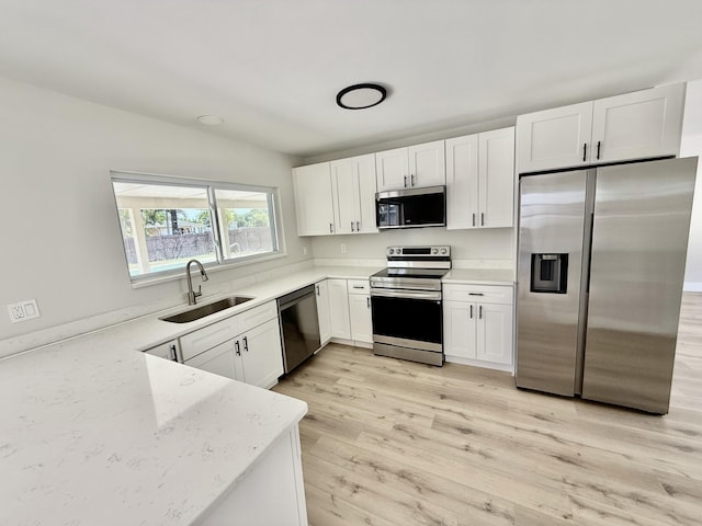 kitchen with white cabinets, light stone countertops, appliances with stainless steel finishes, a sink, and light wood-style floors