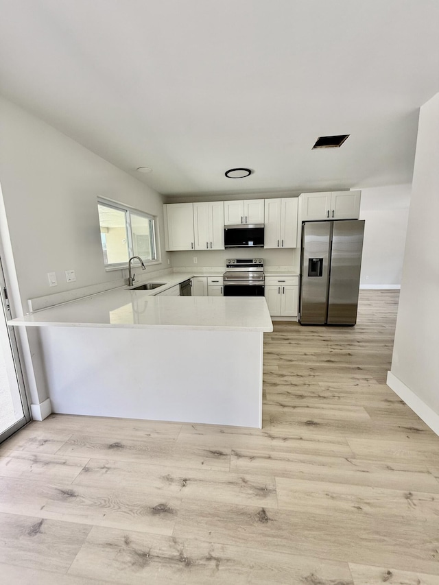 kitchen with white cabinets, a sink, light wood finished floors, light countertops, and stainless steel appliances