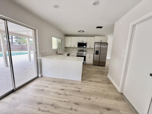 kitchen with white cabinets, stainless steel appliances, light wood finished floors, and light countertops