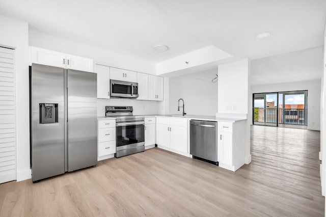kitchen with white cabinets, a sink, light countertops, stainless steel appliances, and light wood-type flooring