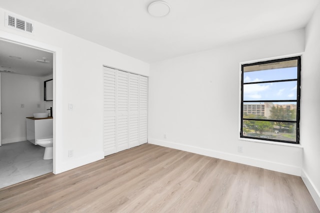 unfurnished bedroom with visible vents, light wood finished floors, baseboards, and a closet