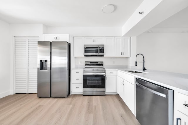 kitchen with a sink, light wood-style flooring, appliances with stainless steel finishes, and white cabinetry