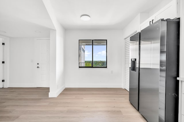 unfurnished bedroom featuring baseboards, light wood-style flooring, a closet, and stainless steel fridge with ice dispenser