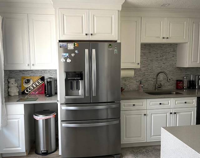 kitchen with white cabinets, stainless steel refrigerator with ice dispenser, decorative backsplash, and a sink