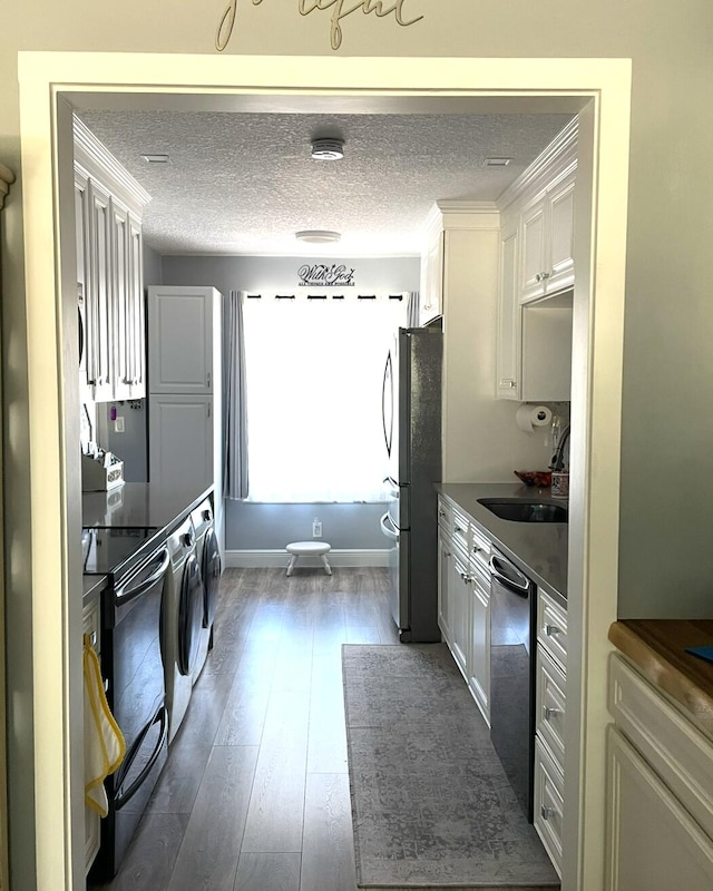 kitchen featuring freestanding refrigerator, dark countertops, dark wood-style floors, a sink, and dishwasher