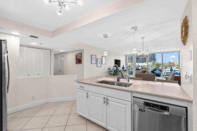kitchen with a sink, stainless steel appliances, light countertops, white cabinets, and a notable chandelier
