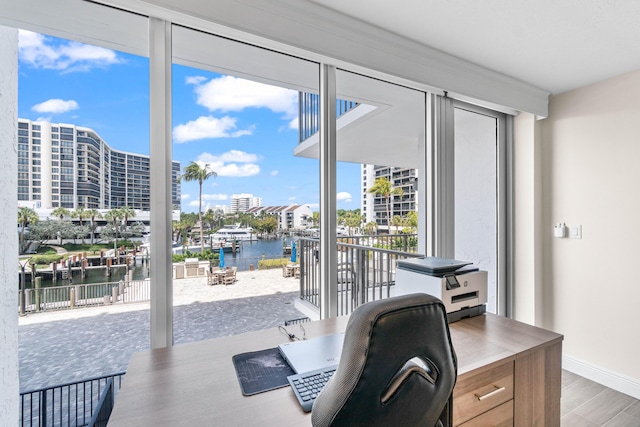 office area with a water view, a wall of windows, baseboards, and wood finished floors