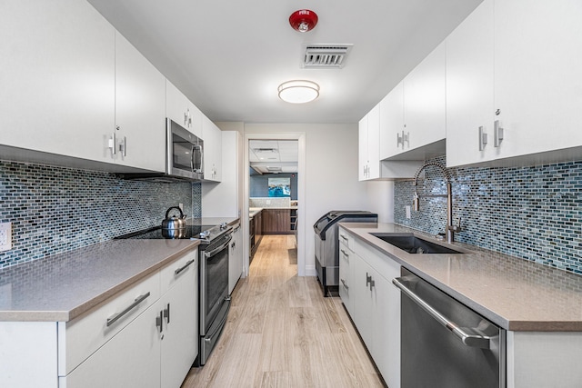 kitchen featuring visible vents, a sink, stainless steel appliances, tasteful backsplash, and light wood-type flooring