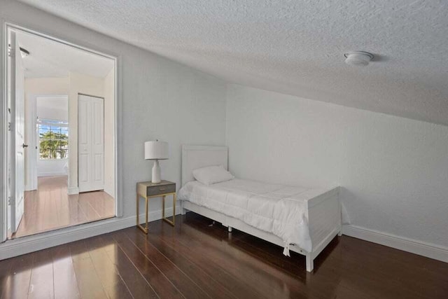 bedroom with a textured ceiling, wood finished floors, and baseboards