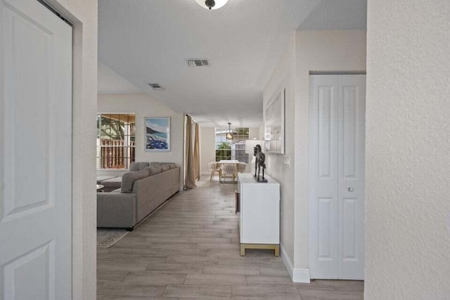 corridor featuring visible vents, a textured wall, and plenty of natural light