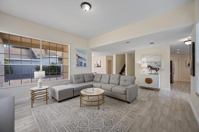 living area featuring light wood finished floors, stairs, and baseboards
