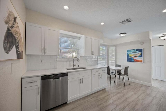 kitchen featuring stainless steel dishwasher, decorative backsplash, light countertops, a sink, and visible vents