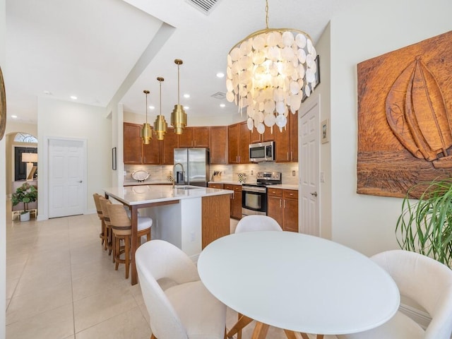 6000 Venetto Way, Vero Beach, FL 32967 - kitchen with an inviting chandelier, stainless steel appliances, decorative backsplash, a center island with sink, and light countertops