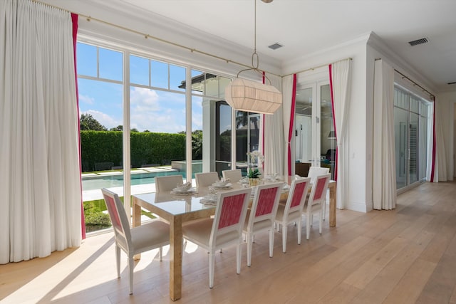 dining area with a healthy amount of sunlight, crown molding, light wood finished floors, and visible vents