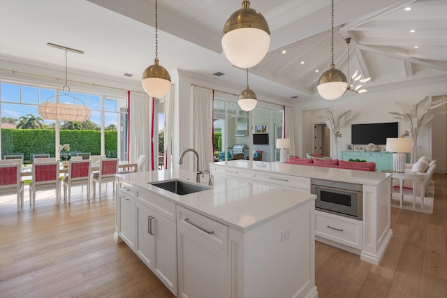 kitchen featuring light wood-style floors, open floor plan, an island with sink, light countertops, and a sink