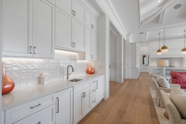 kitchen featuring backsplash, a sink, white cabinets, open floor plan, and light wood-style floors