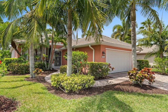 view of front of property featuring driveway, a tile roof, an attached garage, stucco siding, and a front lawn