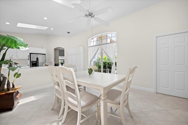 dining space with arched walkways, a ceiling fan, light tile patterned flooring, and a skylight