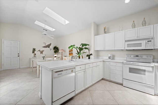 kitchen featuring a peninsula, white appliances, vaulted ceiling with skylight, a sink, and light tile patterned floors