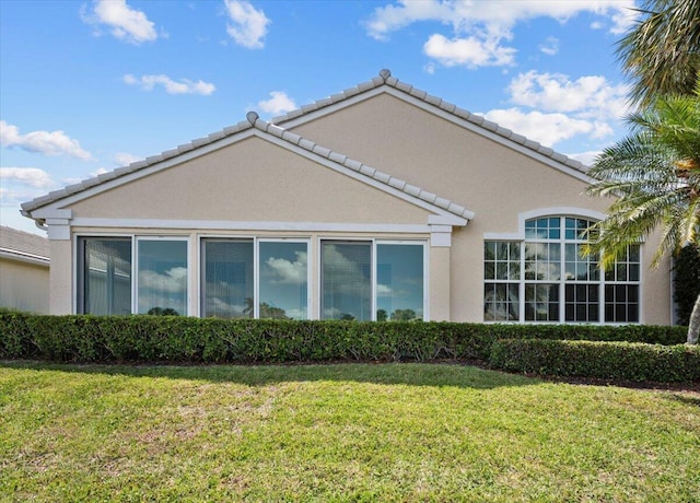 view of side of property featuring a lawn, stucco siding, and a tiled roof