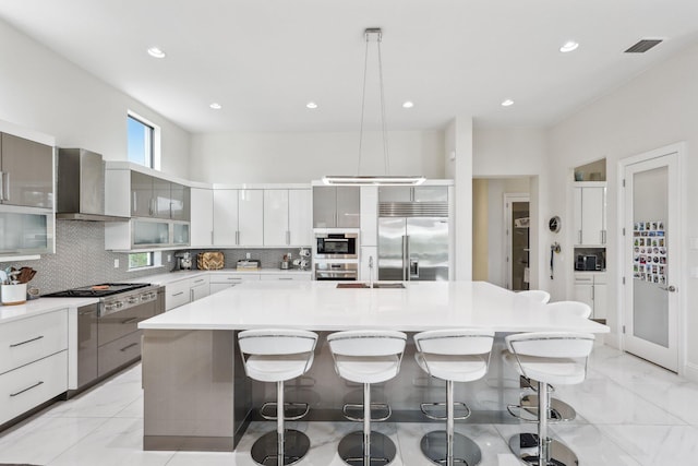 7339 NW 28th Way, Boca Raton, FL 33496 - kitchen featuring tasteful backsplash, stainless steel appliances, marble finish floor, wall chimney exhaust hood, and a kitchen breakfast bar